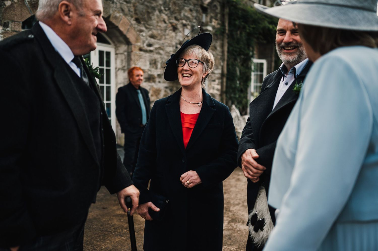 Wedding guests mingling and chatting outside stone building during reception.