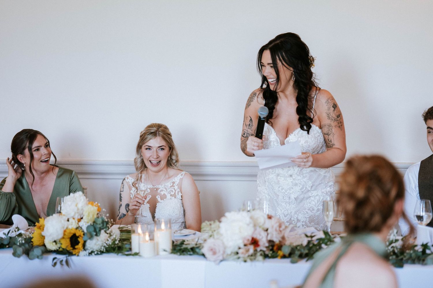 Wedding party members share emotional moments during reception speeches at decorated head table.