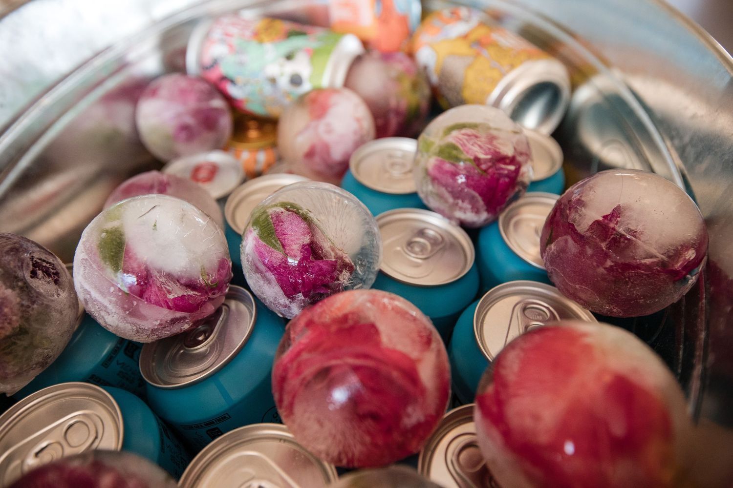 Colorful drinks with pink and red garnishes served in glass containers on ice.