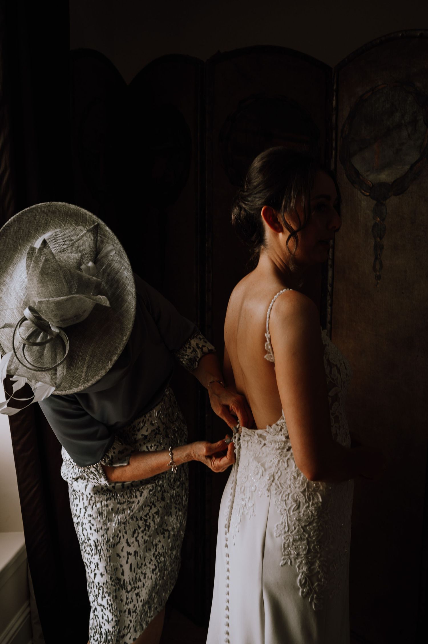 Aberdeen Wedding Photography. Close-up of someone helping with wedding dress buttons in dramatic lighting.