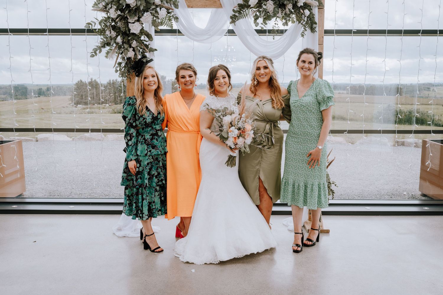 Wedding party in colorful dresses poses by window in modern bright venue.