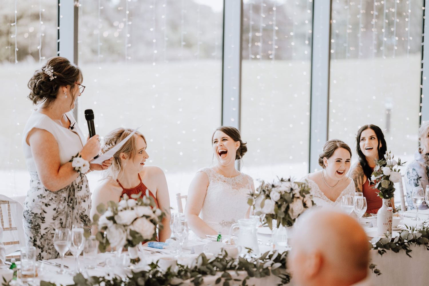 Wedding reception speech moment at head table decorated with floral garlands.