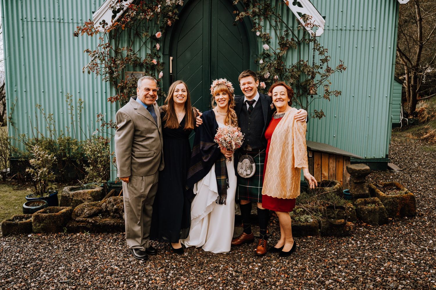 Small wedding group gathers for a photo by the mint green church door with vine decorations.