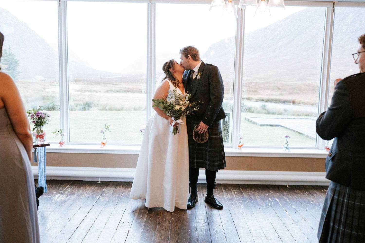 A couple shares a romantic kiss during their first dance in a bright, sunlit reception venue with scenic windows.