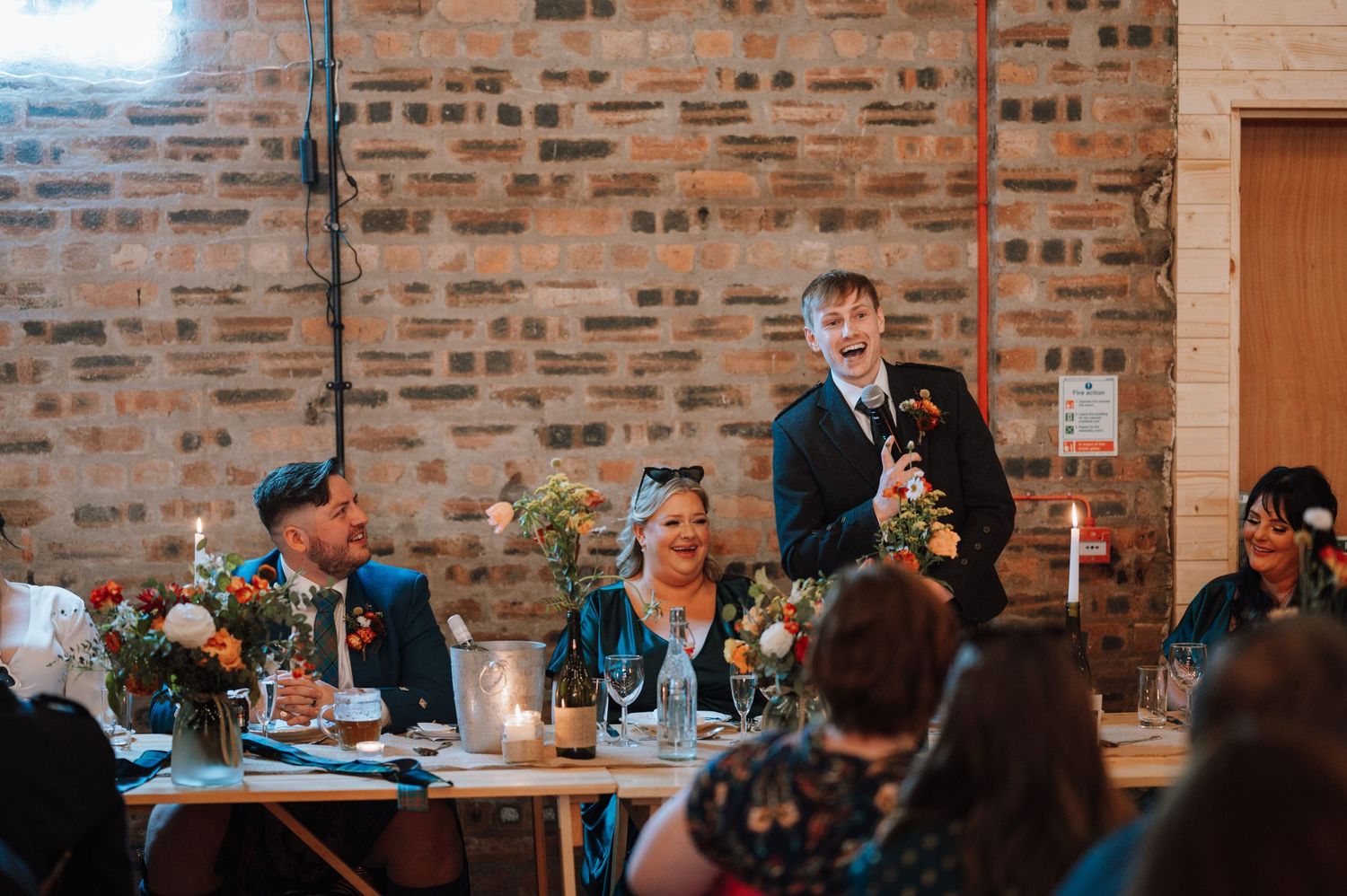 Wedding reception speeches and toasts in rustic brick venue with candlelit tables.