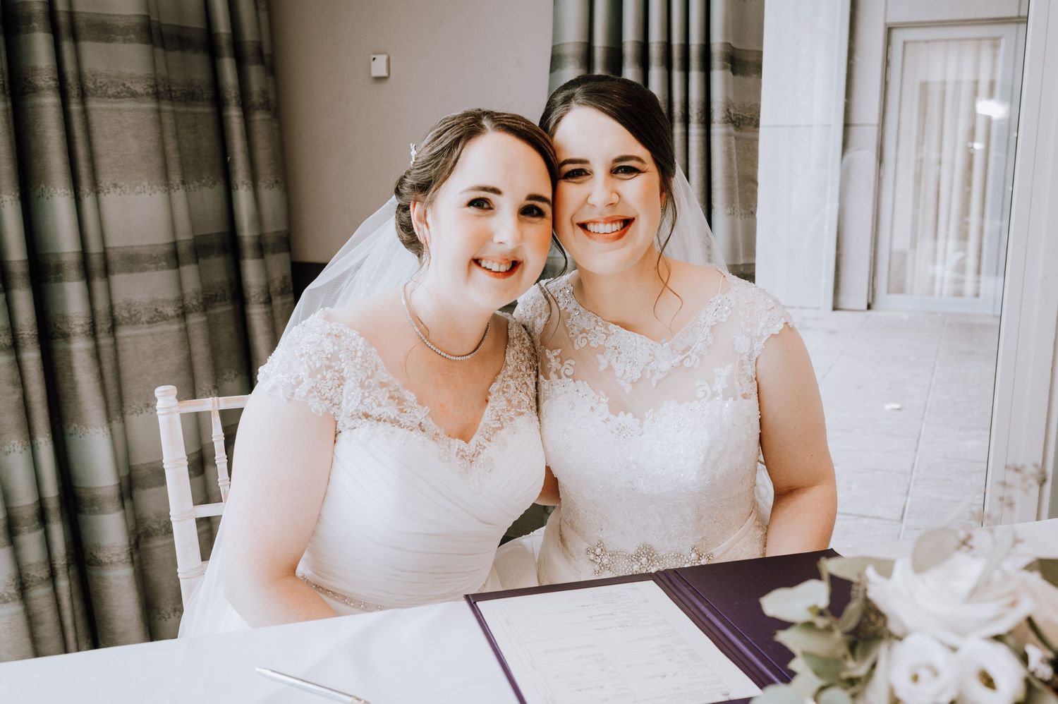 A joyful wedding moment captured as two people smile while seated at a signing table.