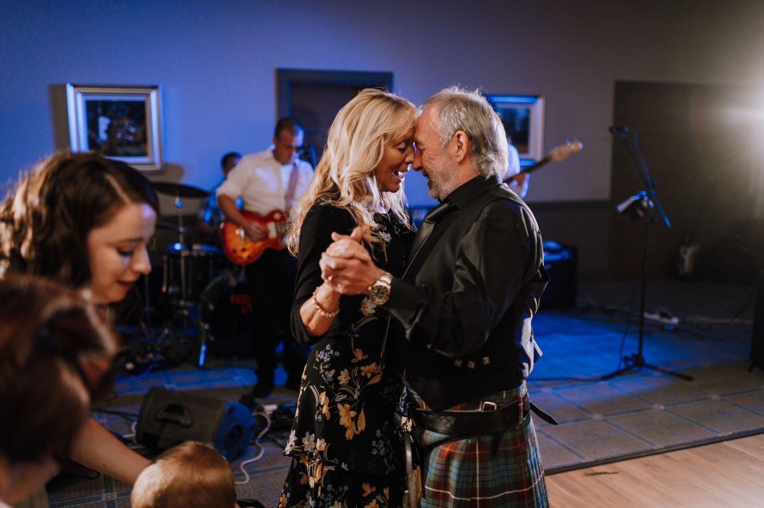 Guests dance together at a wedding reception with a live band performing in the background.