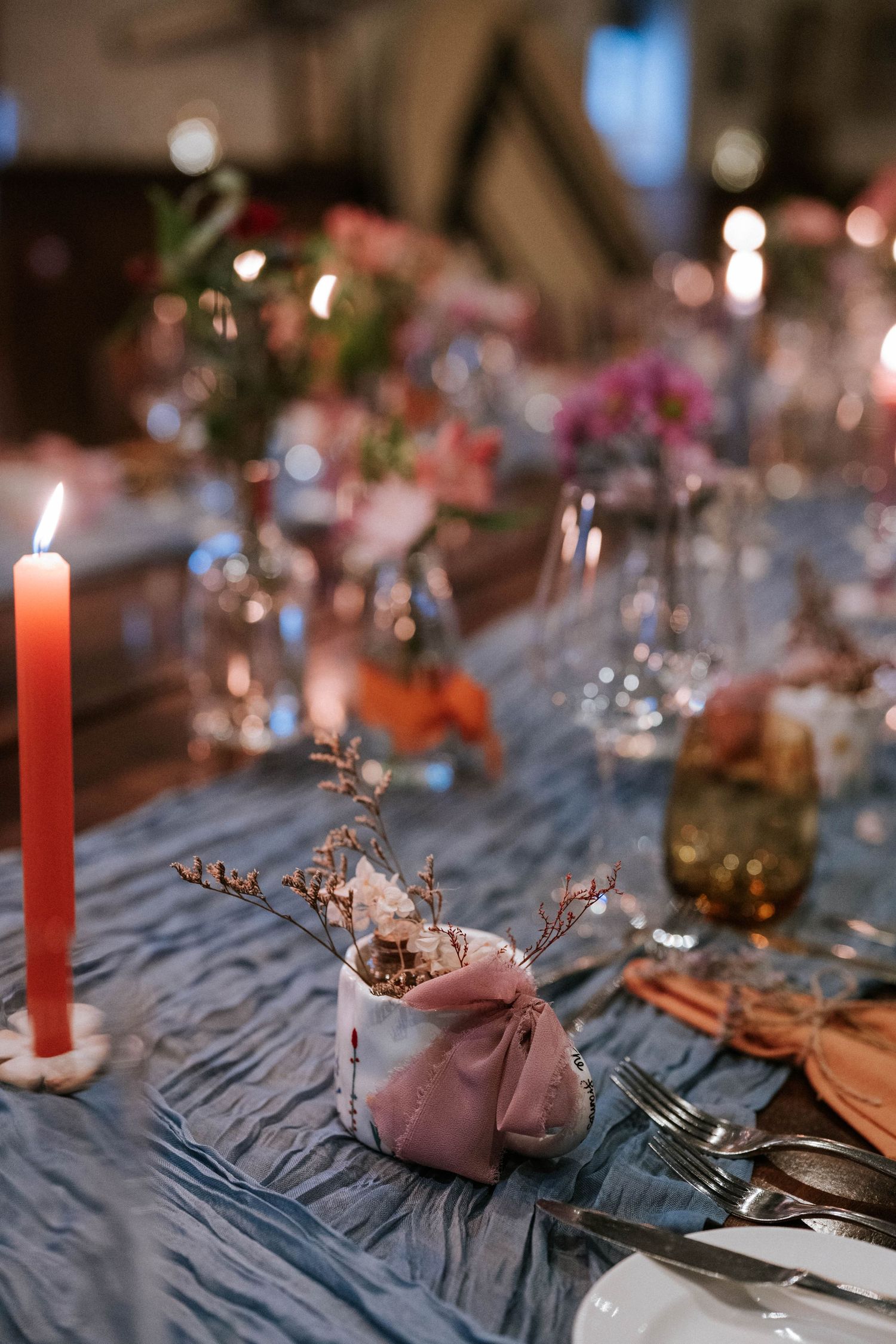 An elegant wedding table setting with red candles, glassware and pink napkins on blue tablecloth.