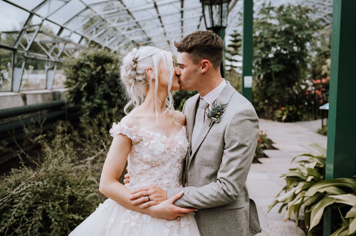 Newlyweds share an intimate moment in a beautiful greenhouse setting.