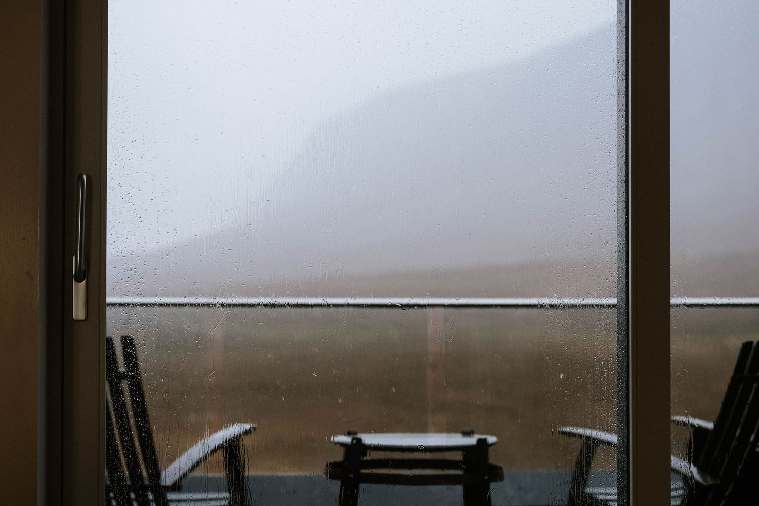 A misty mountain view through large windows with empty chairs in the foreground.