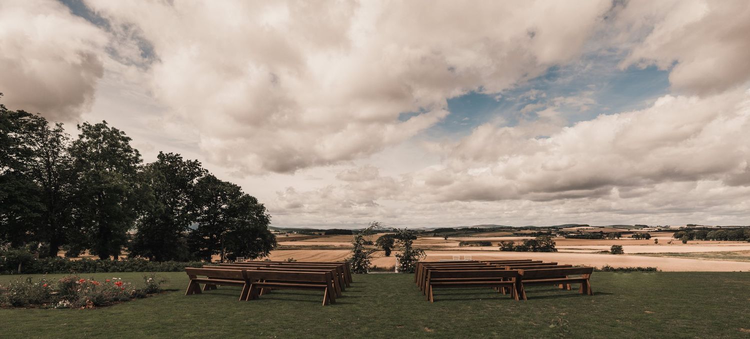 Scenic rural landscape with wooden benches overlooking rolling fields under dramatic cloudy skies.