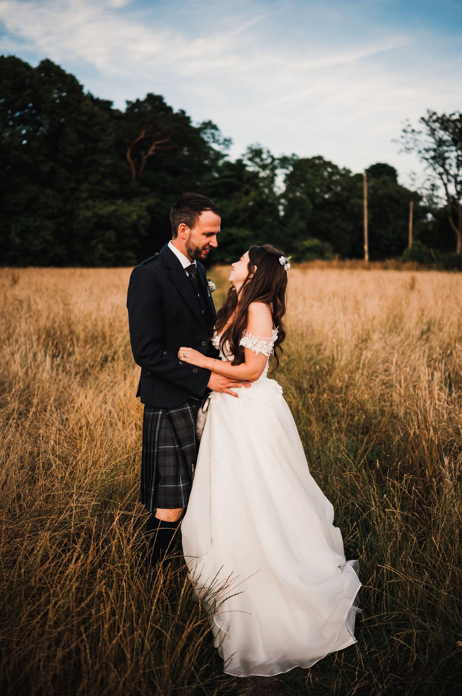 A couple in wedding attire embraces in a golden field during sunset.