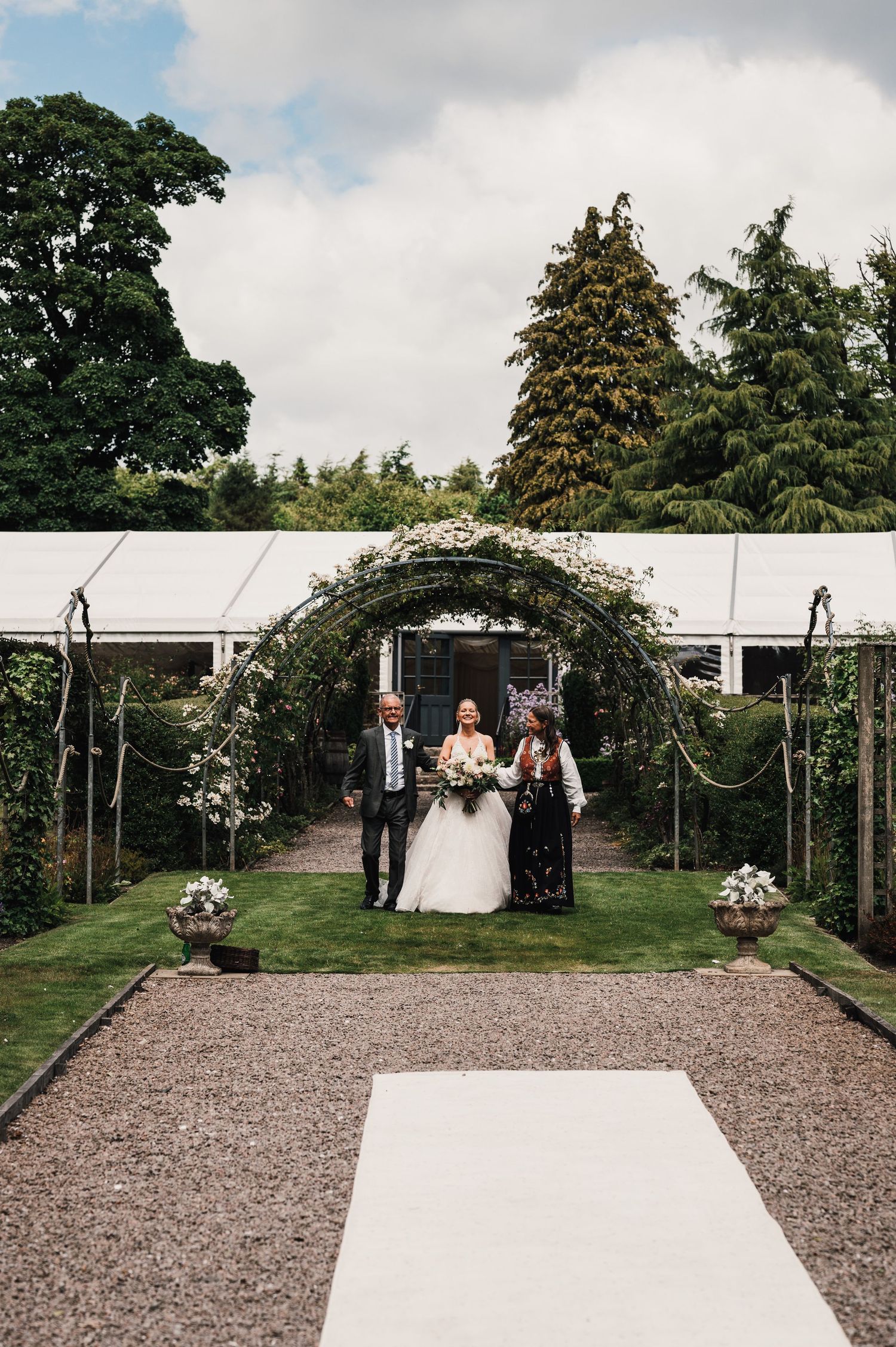 Wedding ceremony setup with floral arch, white aisle runner and garden pathway.