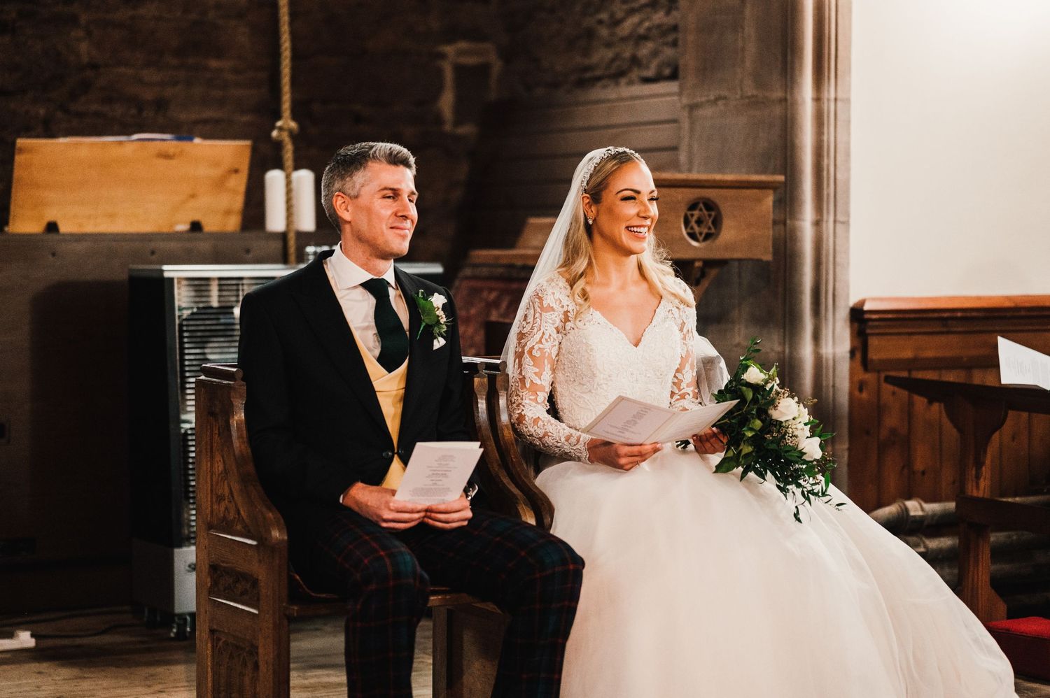 A couple seated during their wedding ceremony in a historic stone church interior.