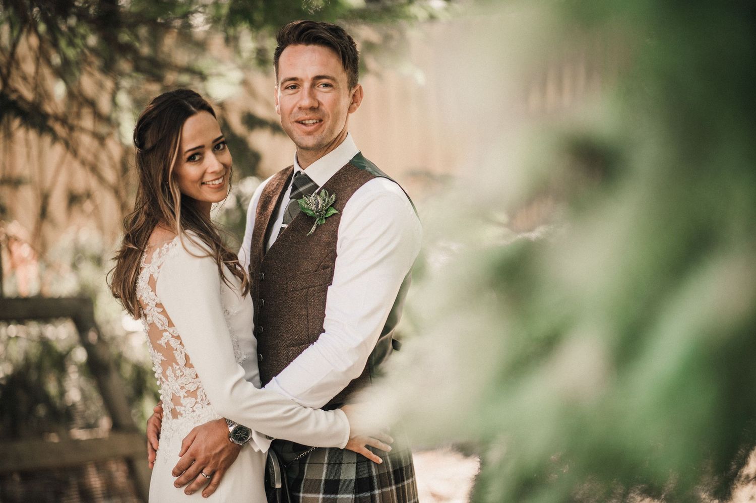 A wedding couple shares a tender moment in soft lighting with green foliage in the background.