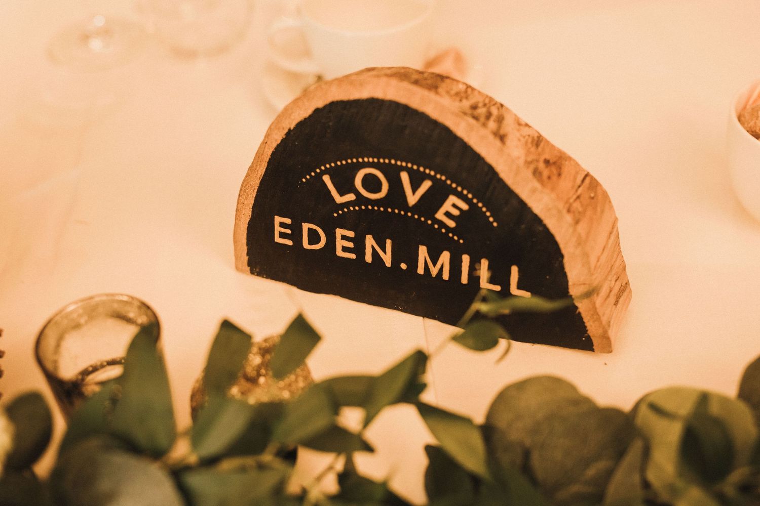 A black and gold 'Love Eden Mill' sign nestled among greenery at an event.
