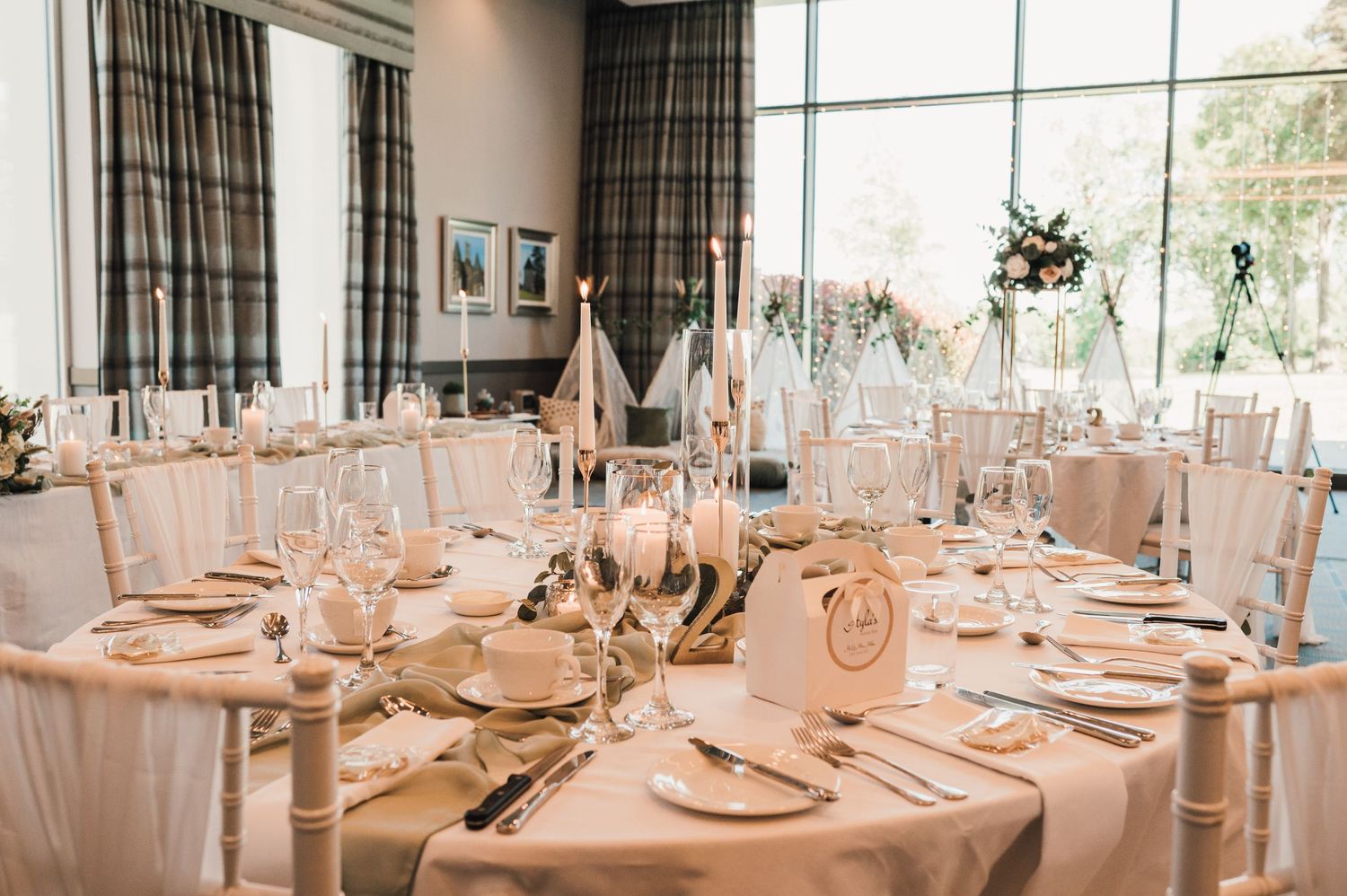 Elegant wedding reception tables set with white linens, fine china, and glassware in a bright banquet room.