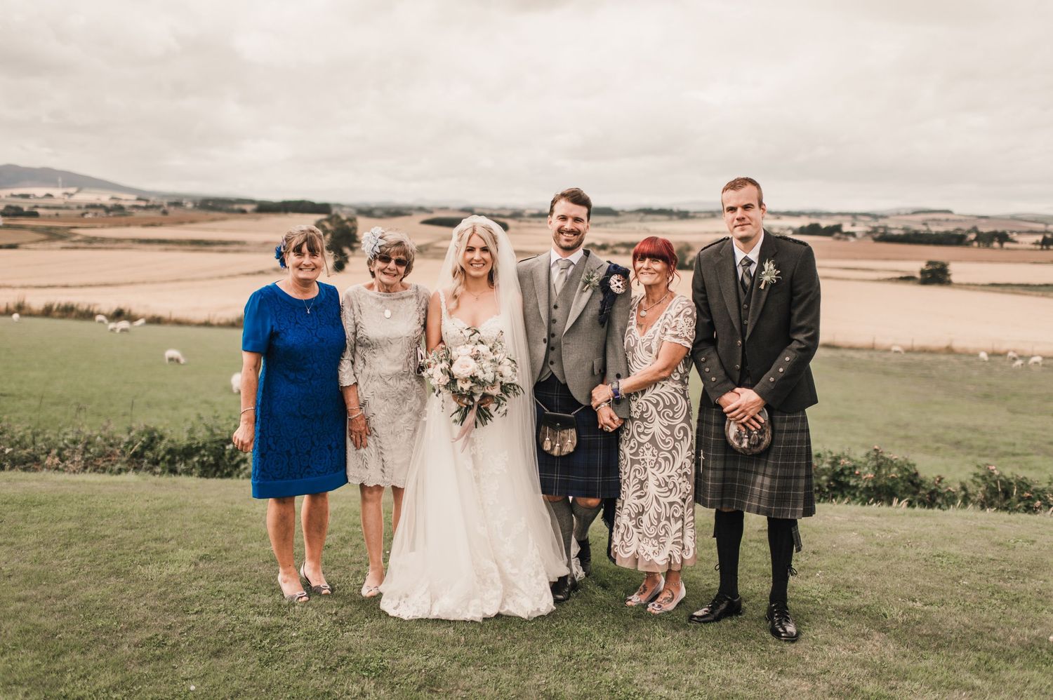 Family members gather for formal wedding portrait overlooking Scottish countryside.