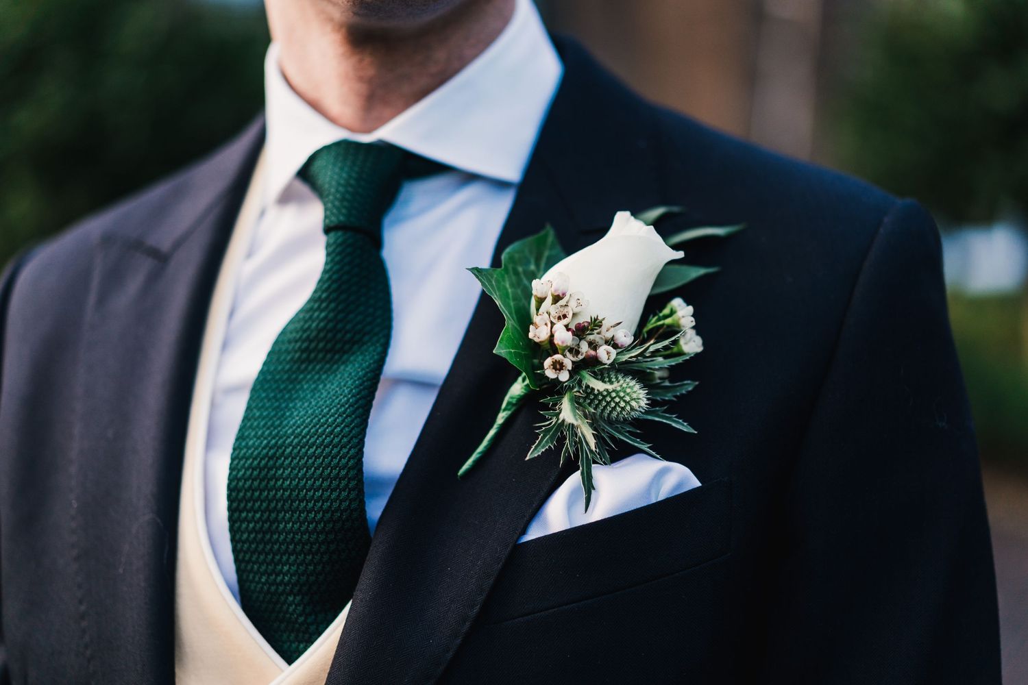 Close-up of emerald green tie and white floral boutonniere on formal suit.