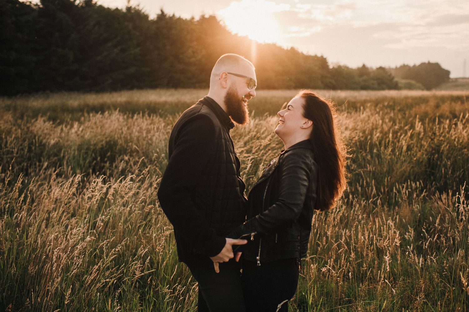 Two people sharing a loving moment in a sun-drenched field with trees in the background.