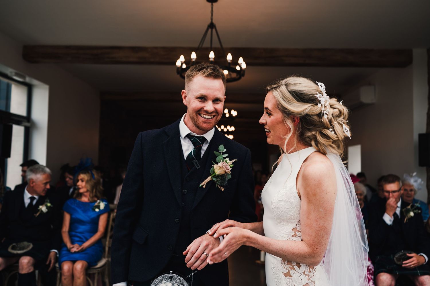 Wedding ceremony moment captured under chandelier lighting in rustic indoor venue.