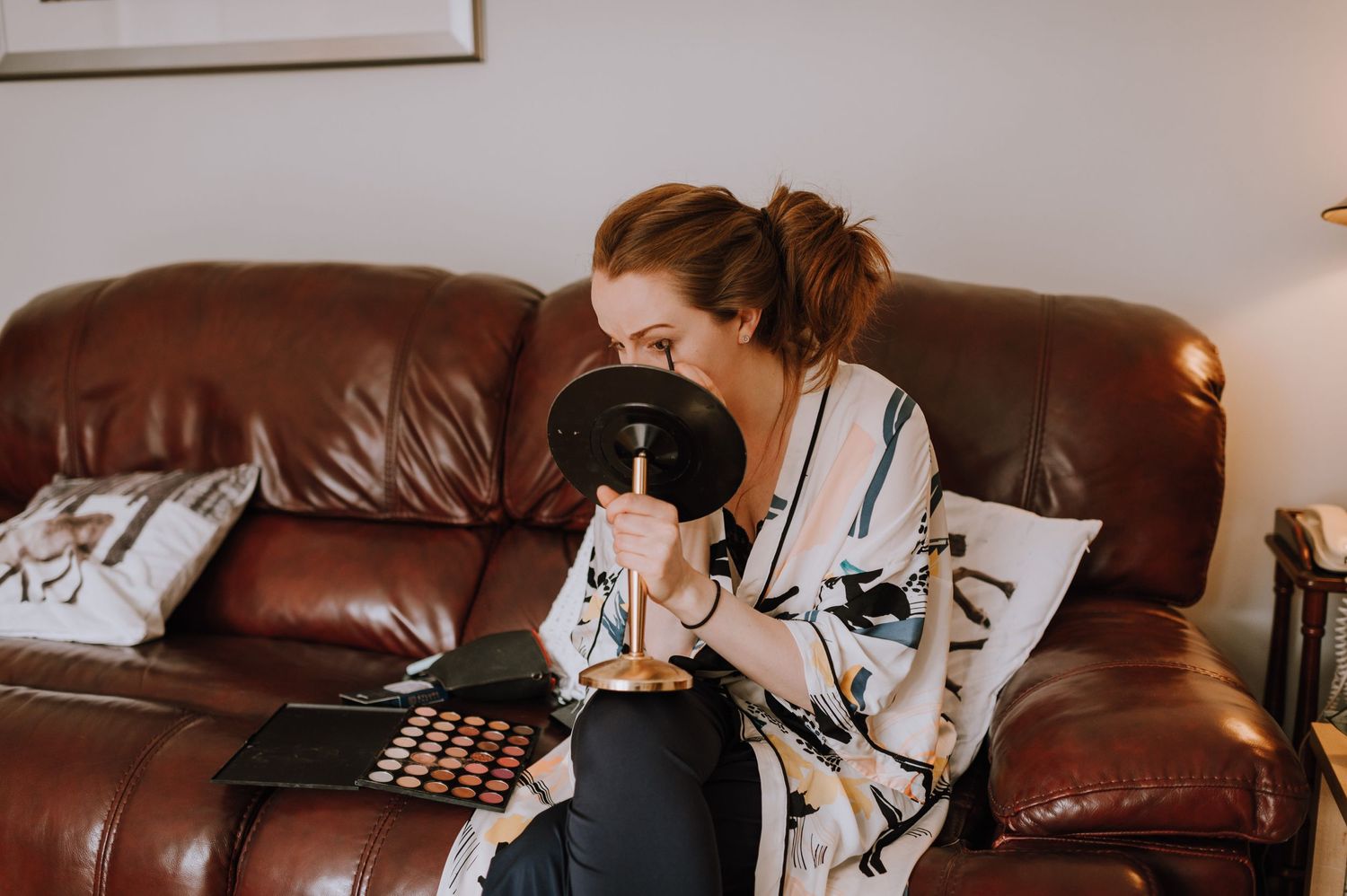 Person sitting on brown leather couch looking at makeup palette.