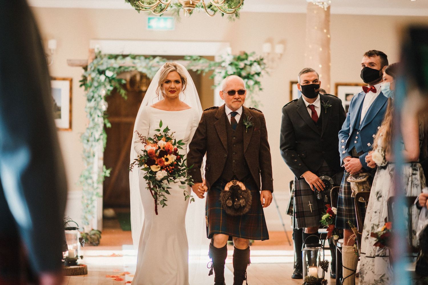 Wedding ceremony features traditional Scottish elements with kilt attire in an elegant indoor setting.