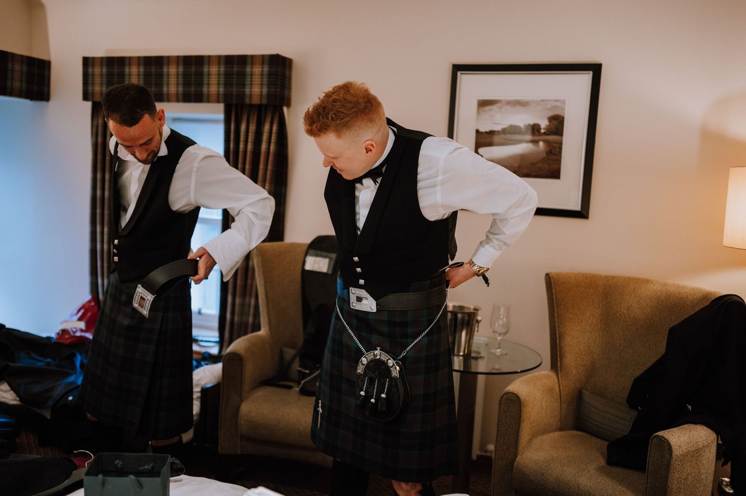 Groomsmen adjusting traditional Scottish formal wear in a hotel room.