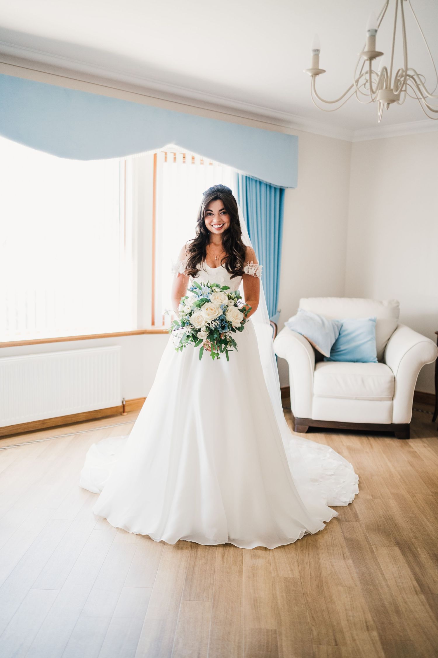 A bride in a classic white gown holds a bouquet in an elegant room with blue accents.