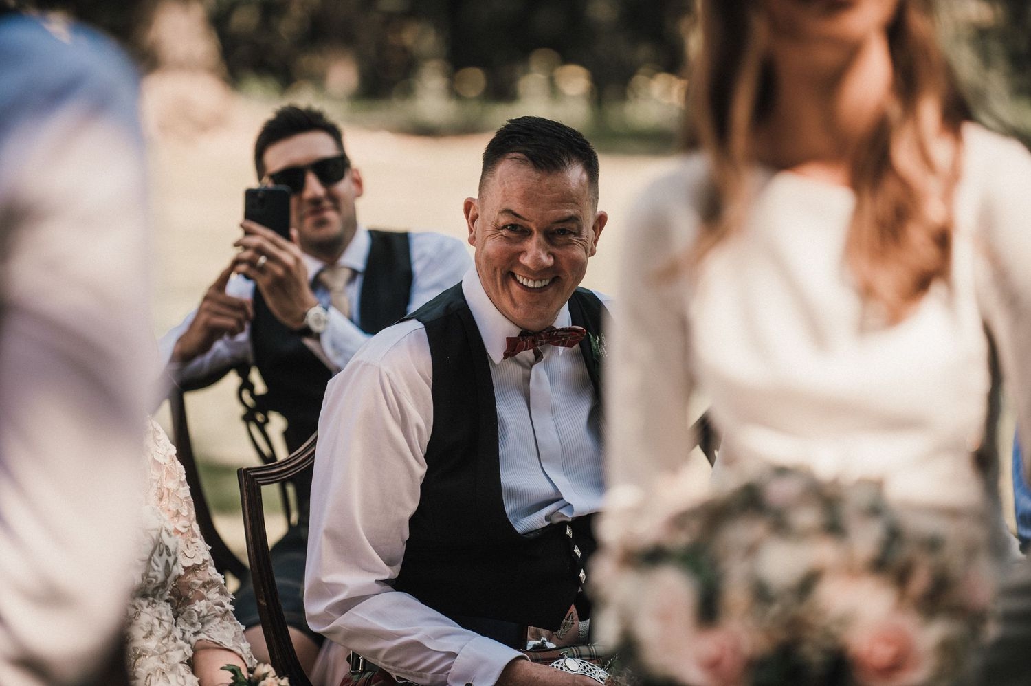 Wedding photographers capture moments during an outdoor ceremony among the trees.