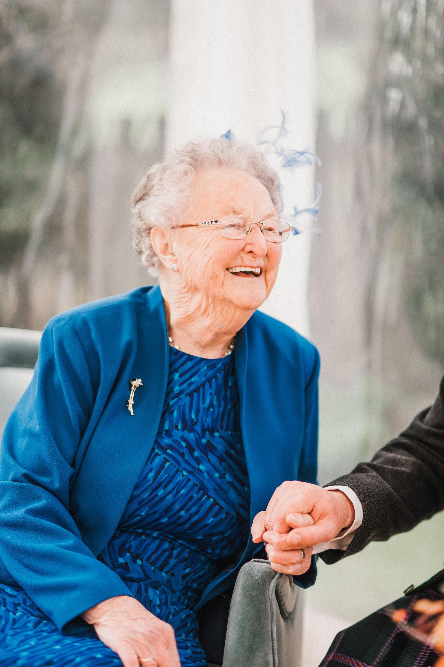 Joyful elderly woman in bright blue outfit smiling during a special occasion.