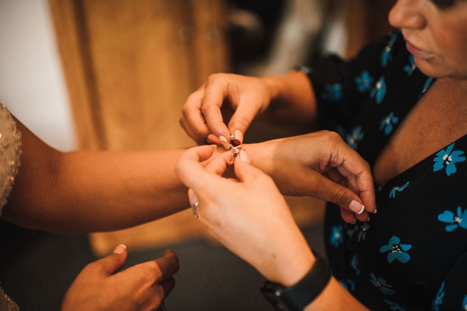 Close-up of hands adjusting jewelry during wedding preparations.