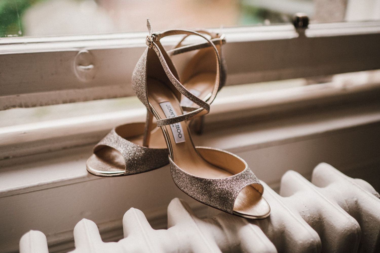 Sparkly silver wedding heels displayed on a white radiator by a window.