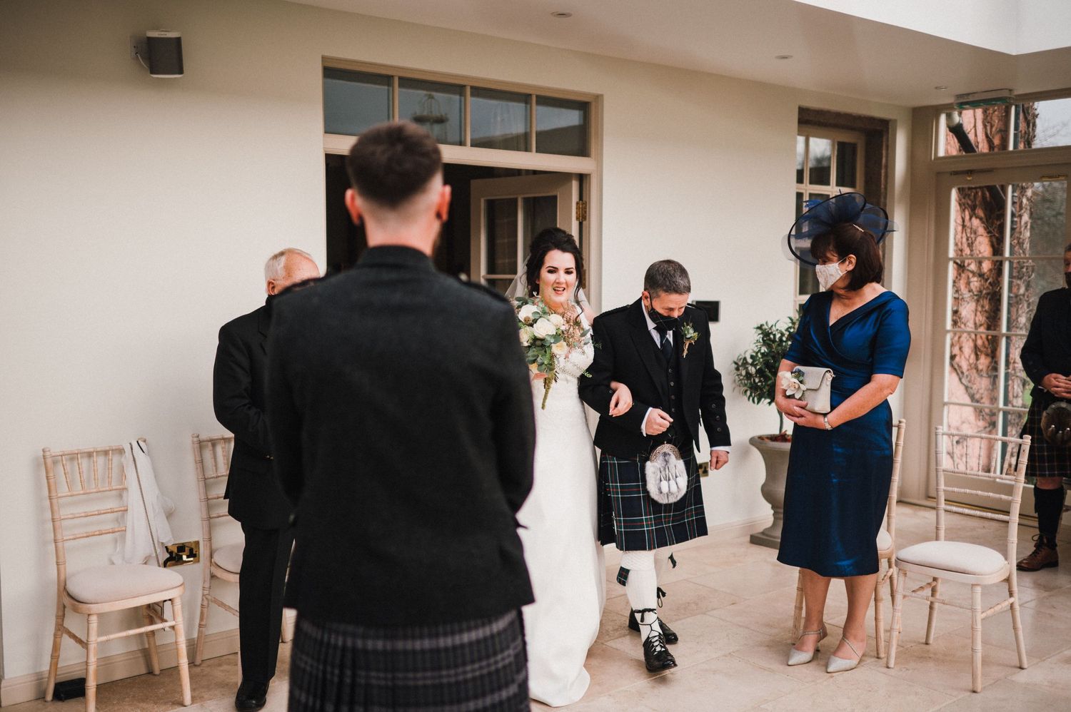 A traditional Scottish wedding ceremony takes place in an elegant indoor venue with kilt-wearing guests.