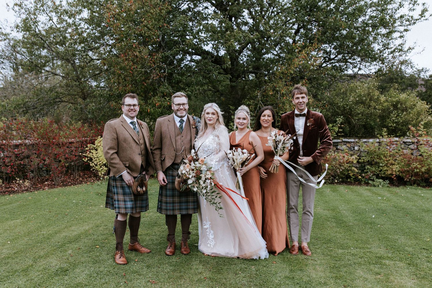 Wedding party gathered on a lush green lawn for formal photographs.