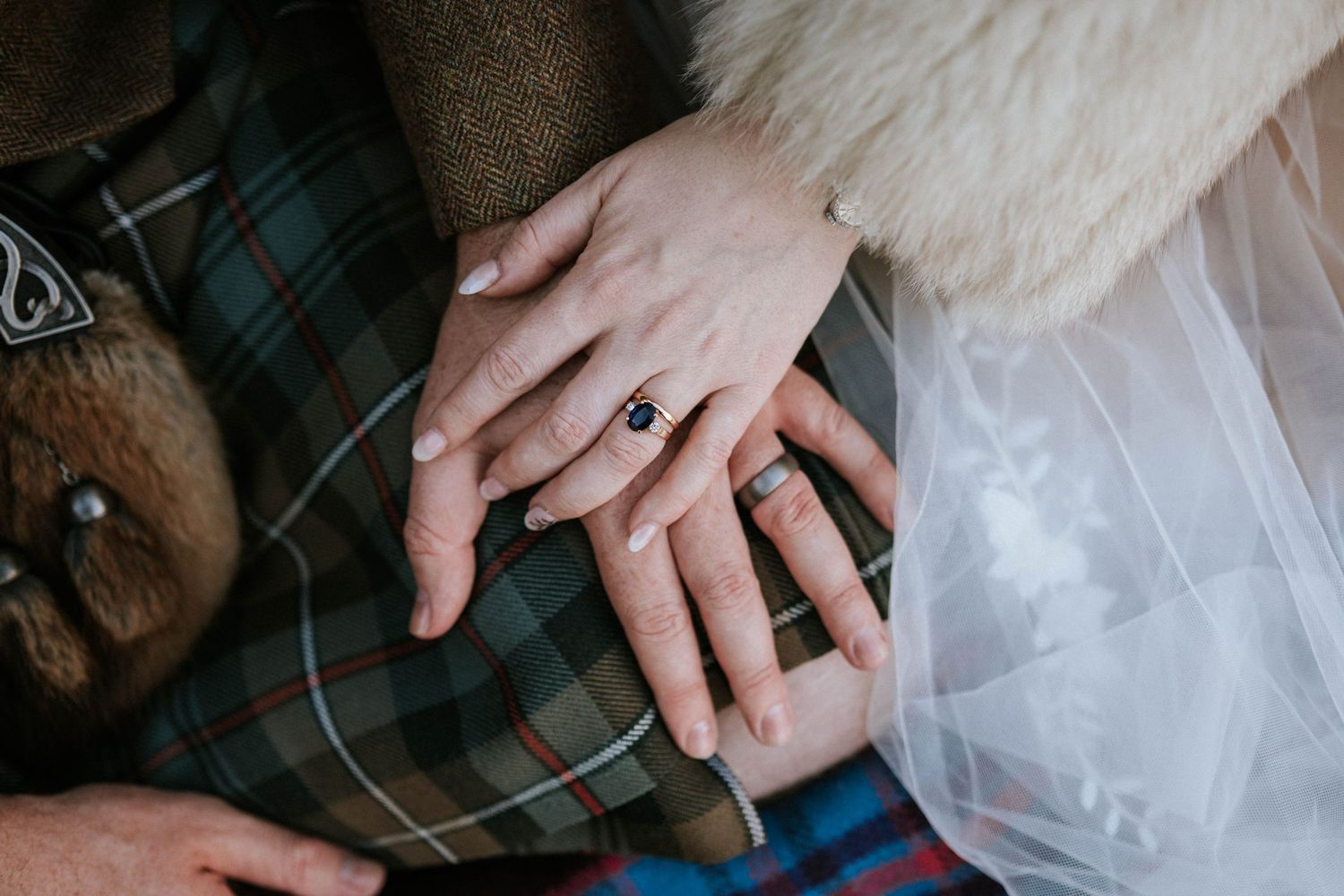 Close-up of hands showing wedding rings against tartan fabric background.