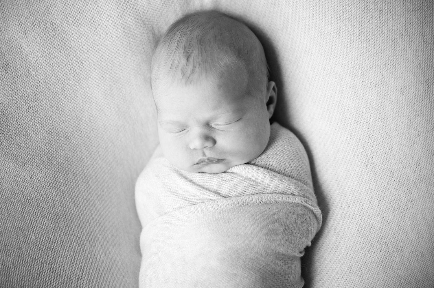 A black and white photo series showing a sleeping newborn baby wrapped in soft swaddling blankets.
