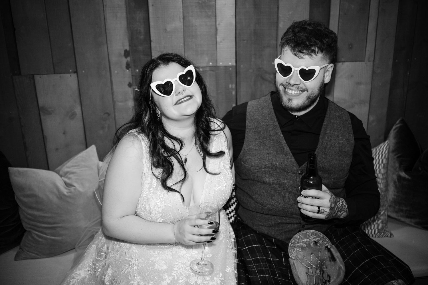 A couple in wedding attire wearing matching heart-shaped sunglasses pose together for a fun photo.