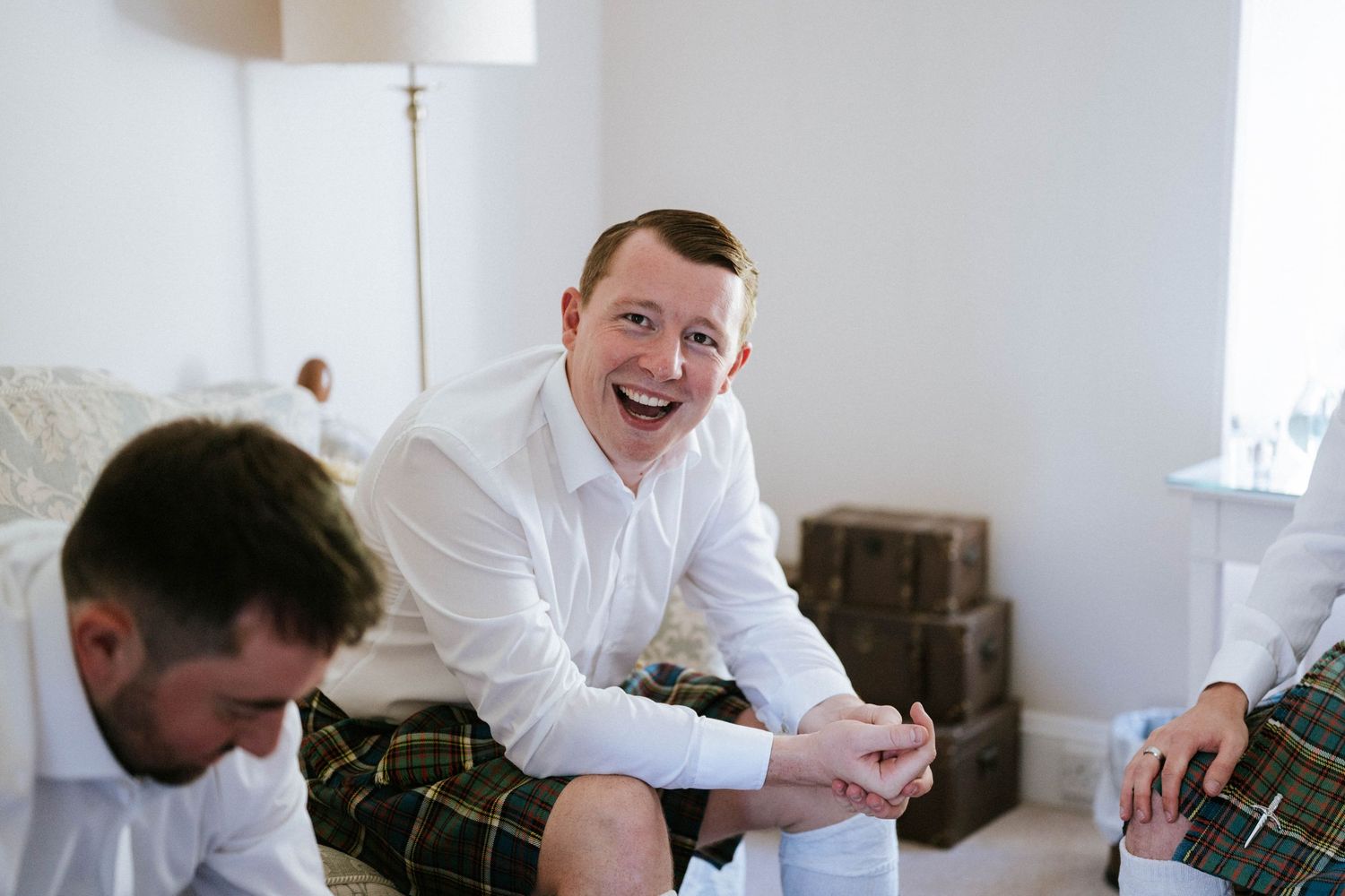 Wedding party members in white shirts and kilts sharing a candid moment.