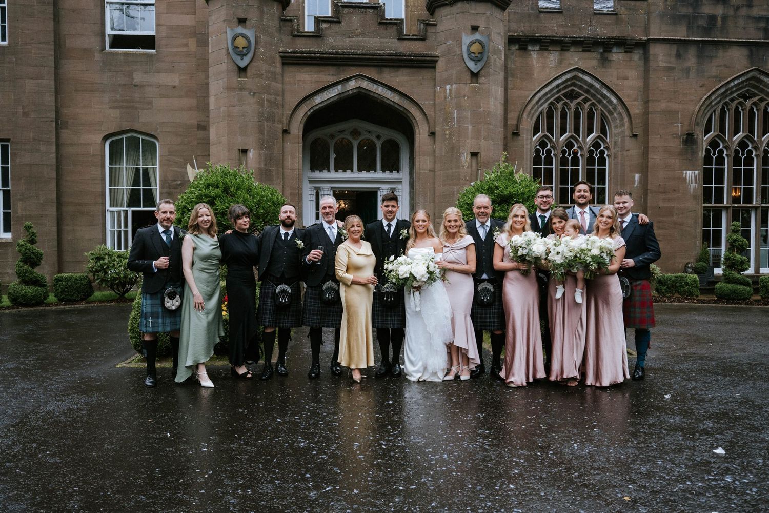 Wedding party poses outside a grand stone building with Gothic architecture details.