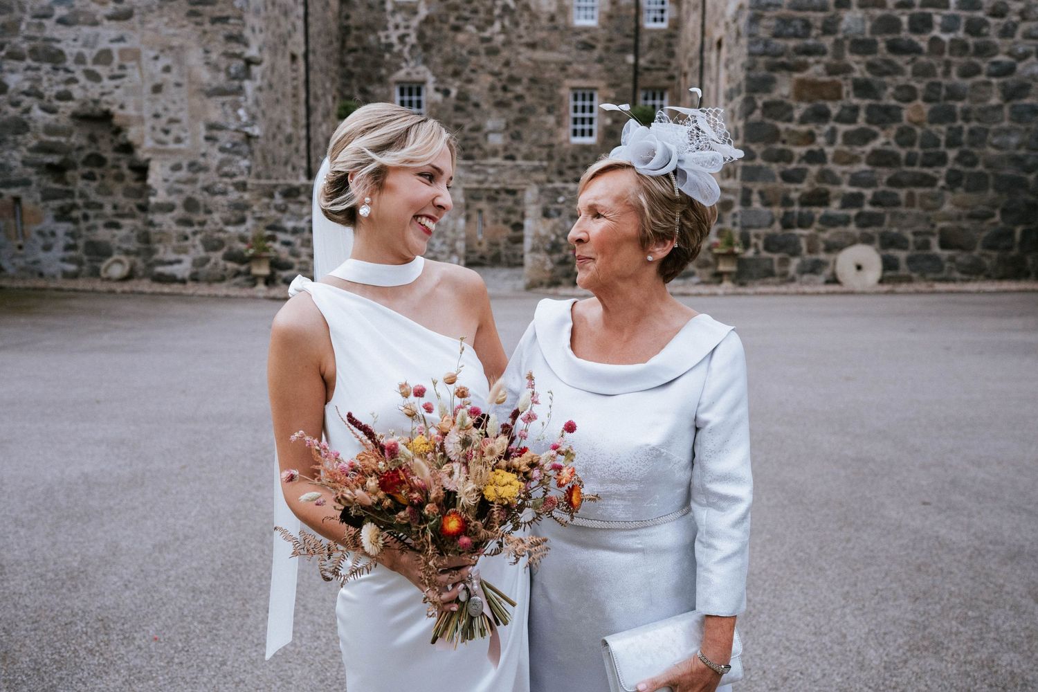 Wedding party members sharing joyful moments outside stone building.