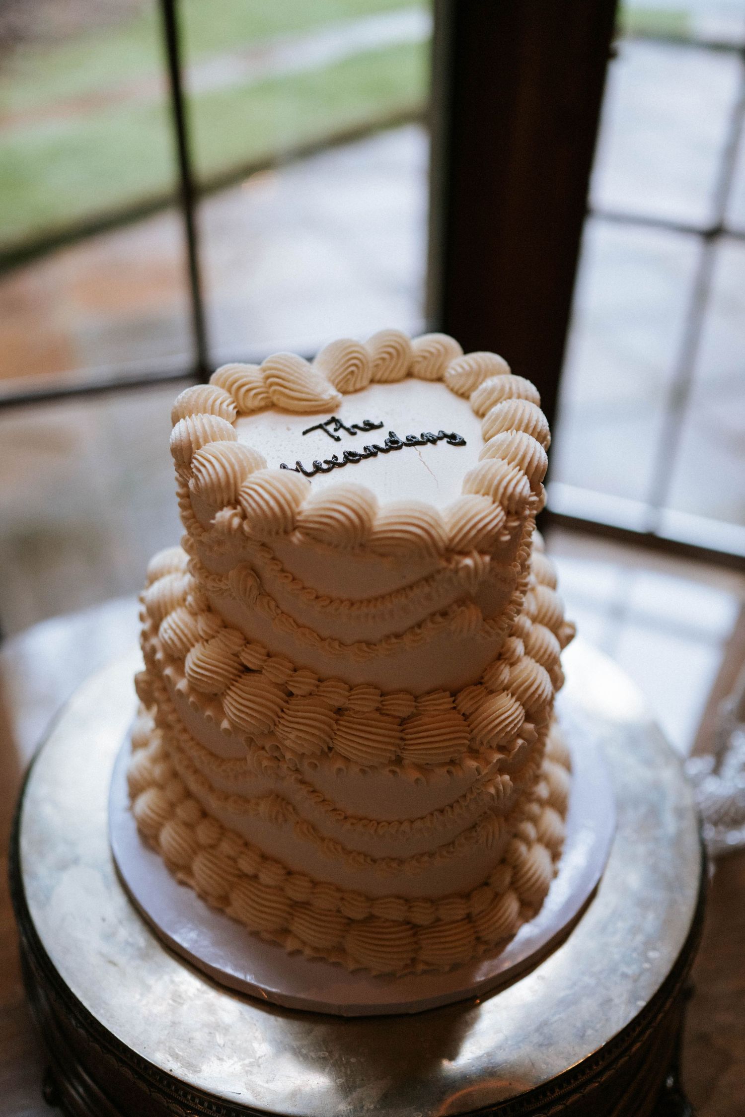 Small wedding cake with delicate beige piped frosting details on silver cake plate.