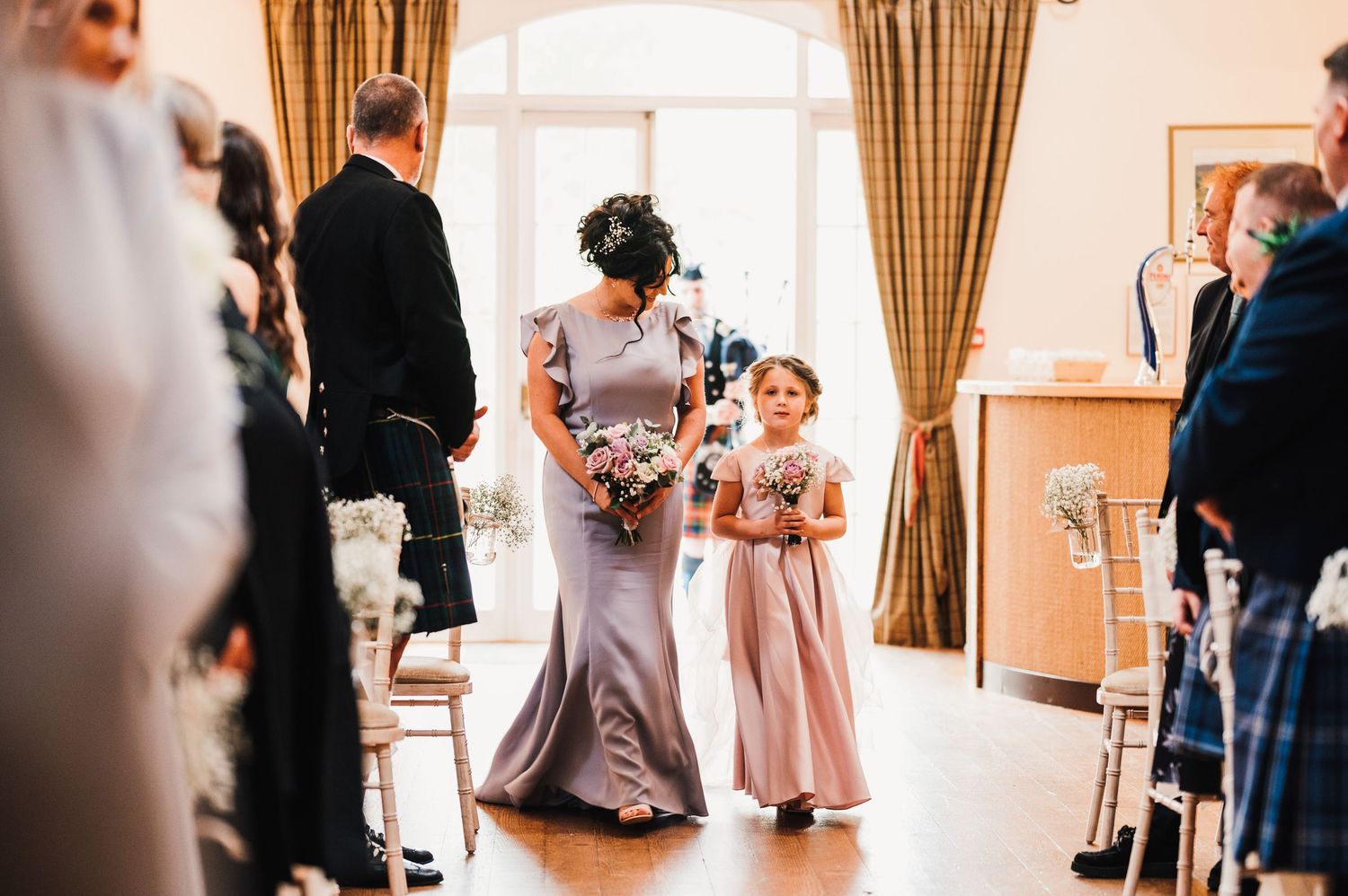 Wedding celebration in progress with guests mingling in an elegant room with tan curtains.