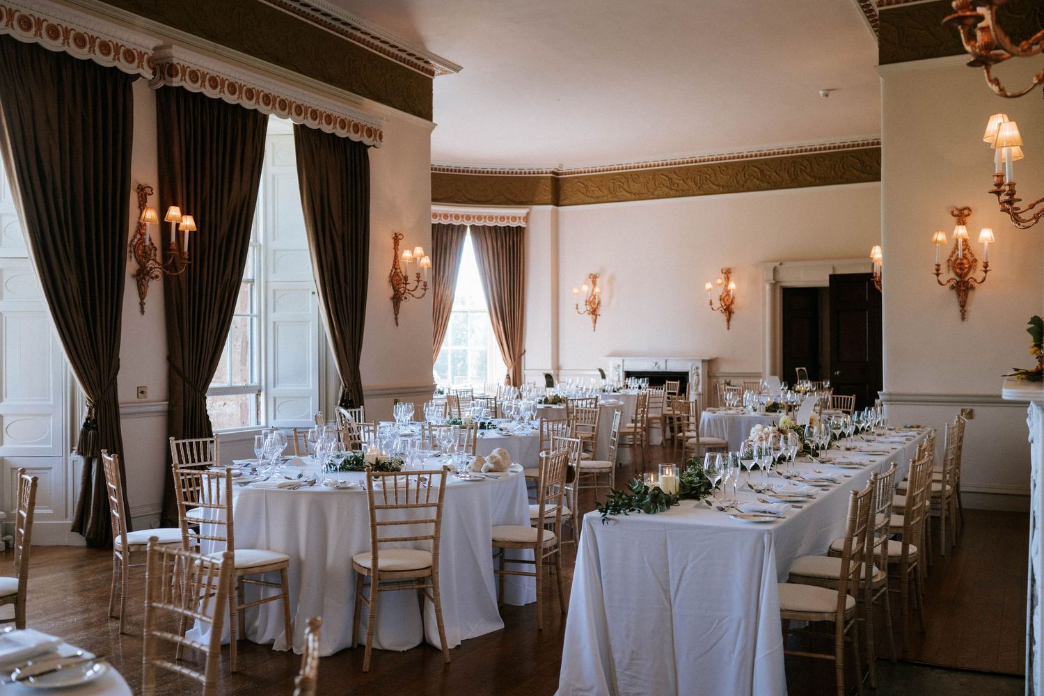 Elegant wedding reception room with white linens and gold chiavari chairs set for dinner.