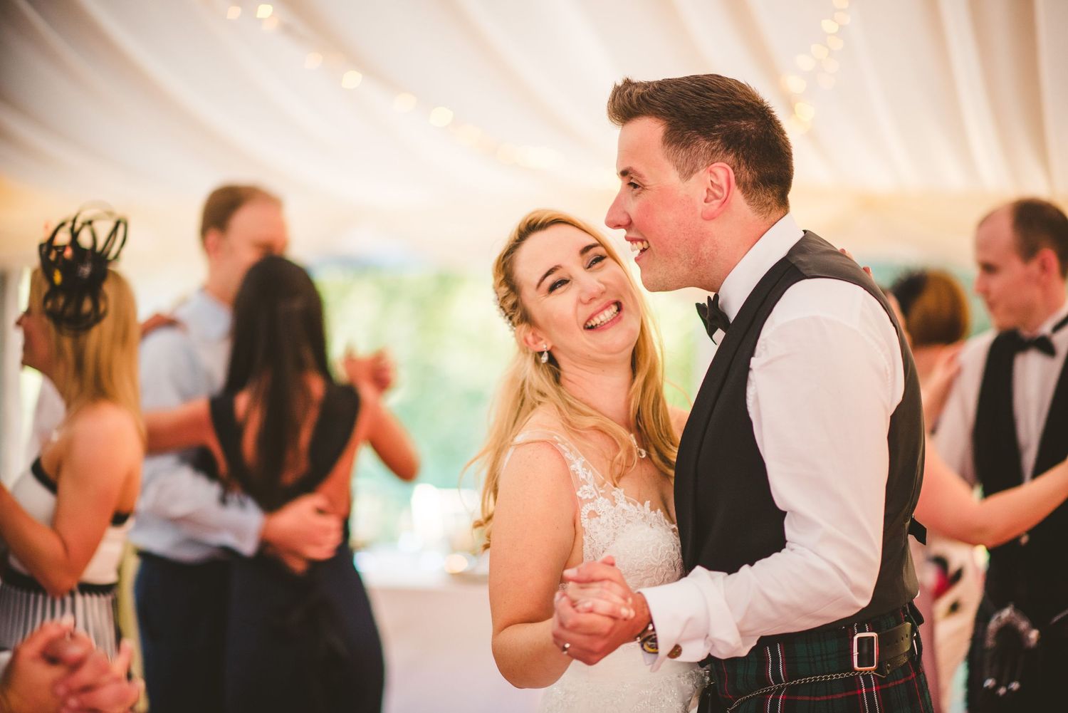 A couple shares a joyful dance moment under a white tent during their wedding reception celebration.