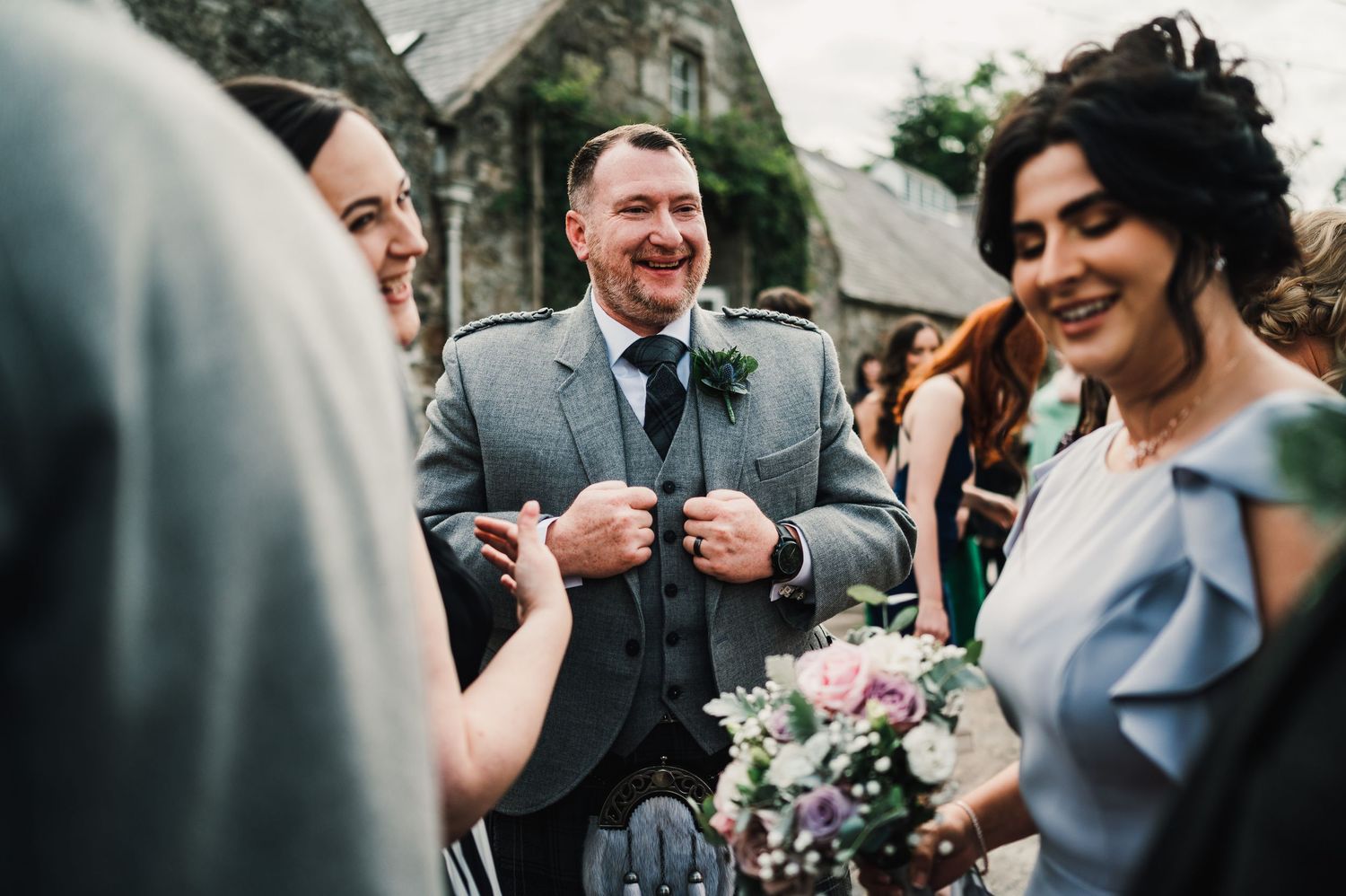 Wedding guests share joyful moments during an outdoor celebration in traditional Scottish attire.
