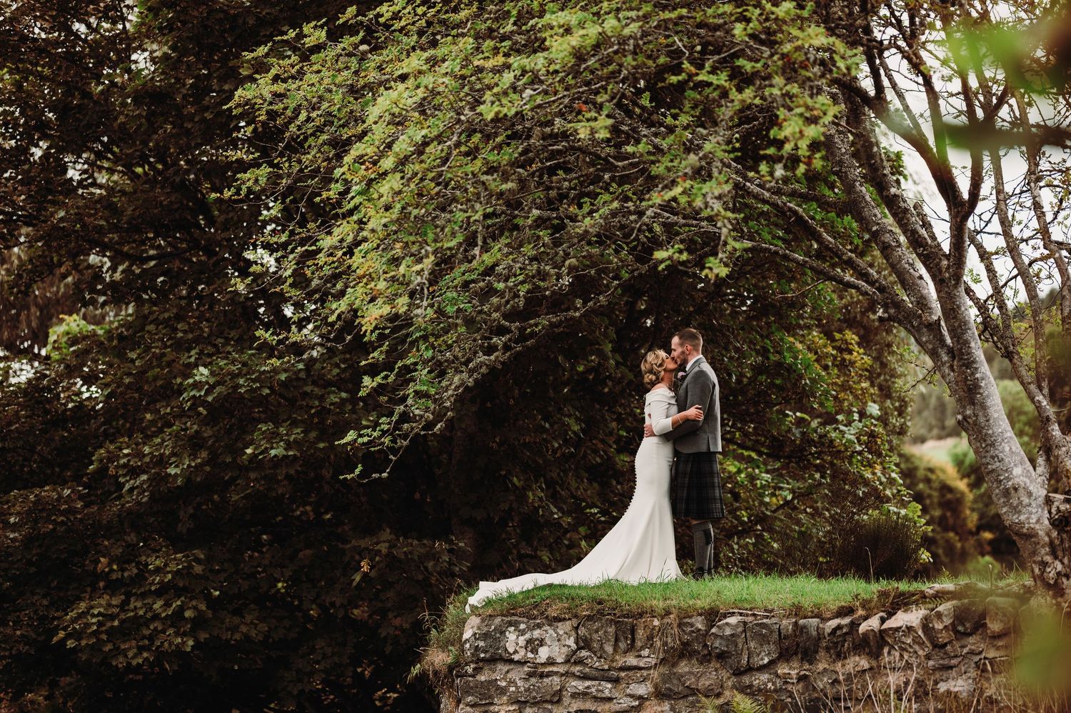 Wedding ceremony taking place in a lush garden setting with trees and greenery.