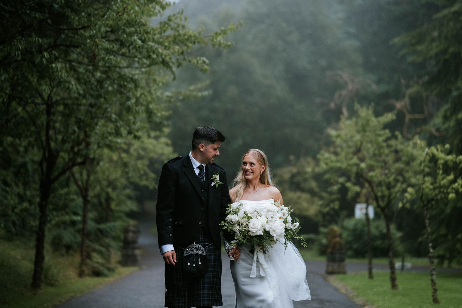 Newlyweds pose for romantic wedding photos in a lush green Scottish landscape.