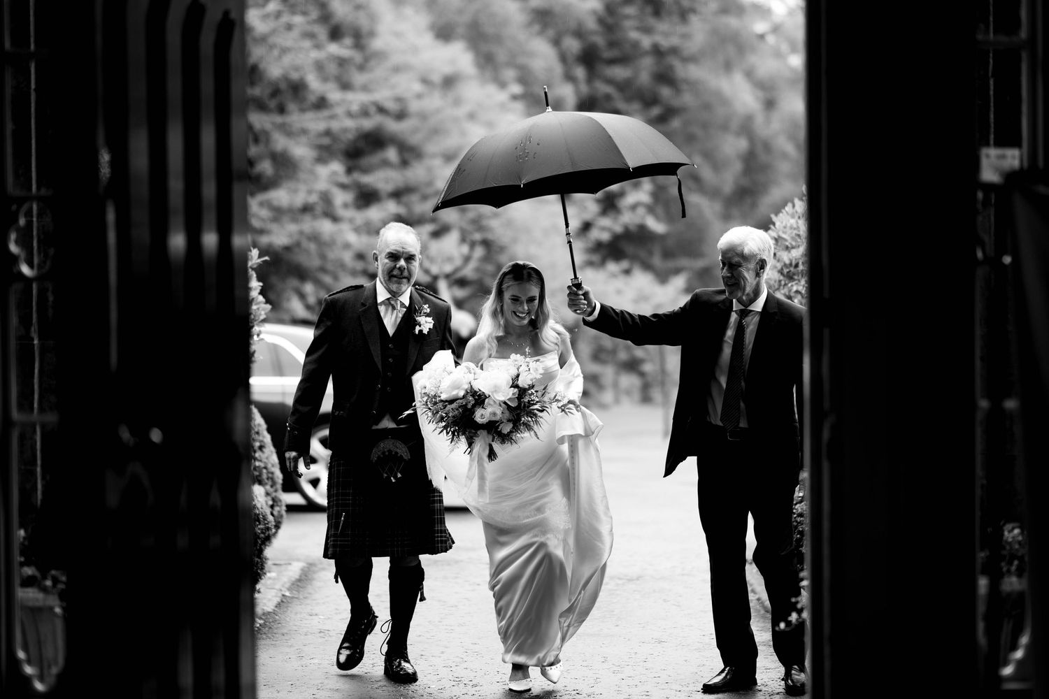 Black and white photo of wedding guests walking with umbrellas in the rain.