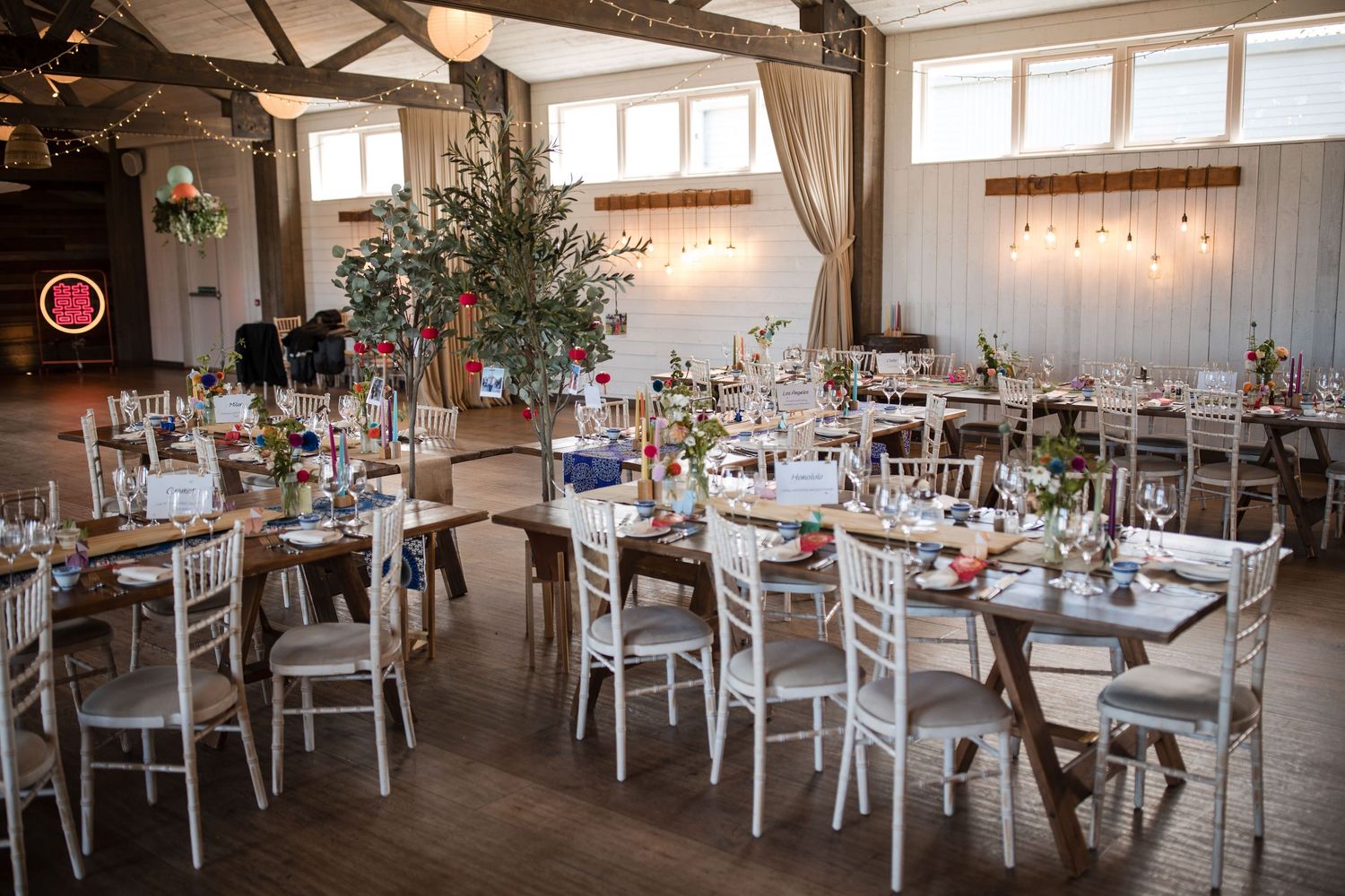 Elegant white wedding reception venue with rustic wooden beams and natural lighting from large windows.